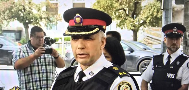 man in a police uniform outdoors speaking at a news conference