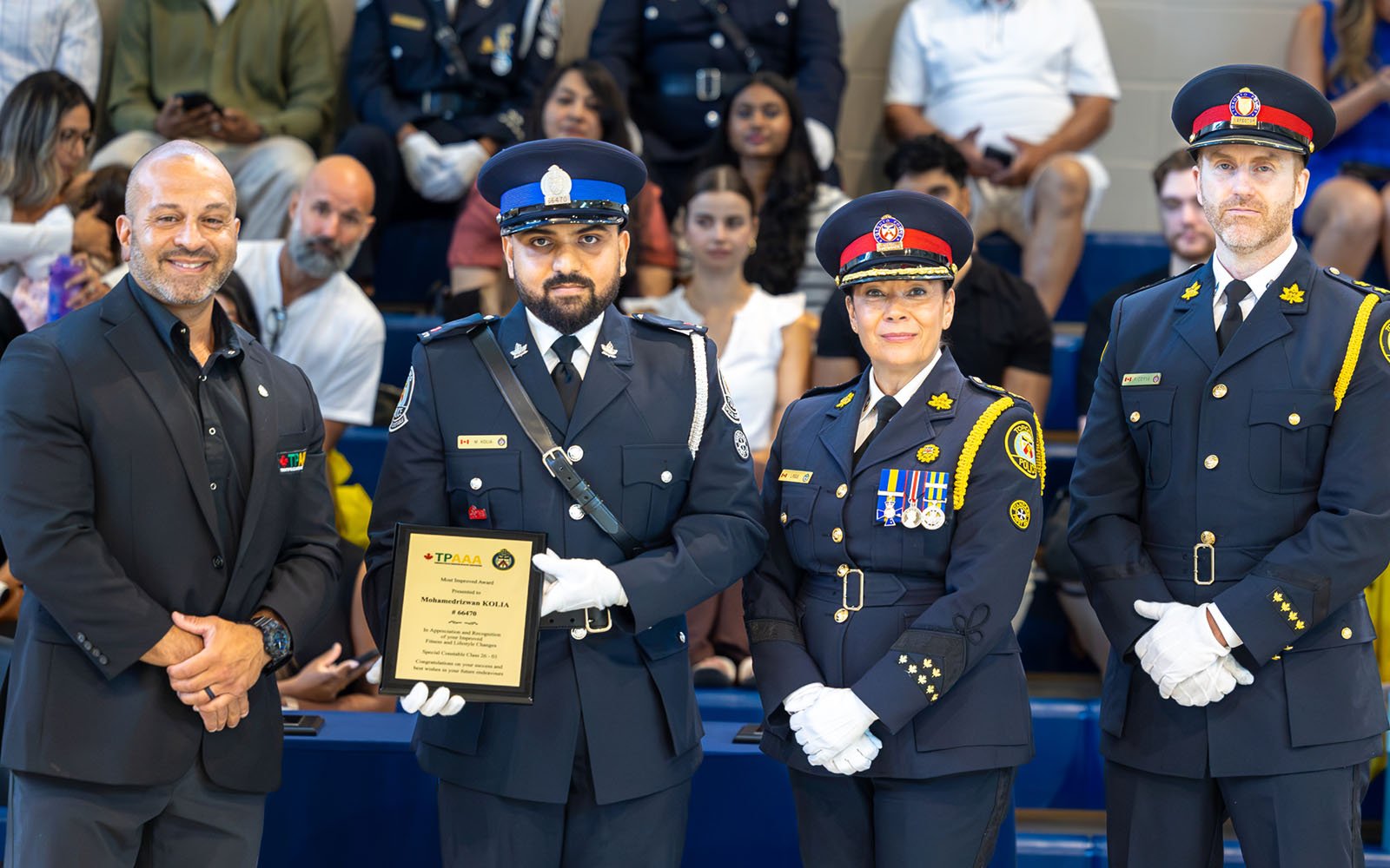 three men (two in police uniforms) and a woman in a police unfirom pose for a photo; a man in the middle is holding a plaque