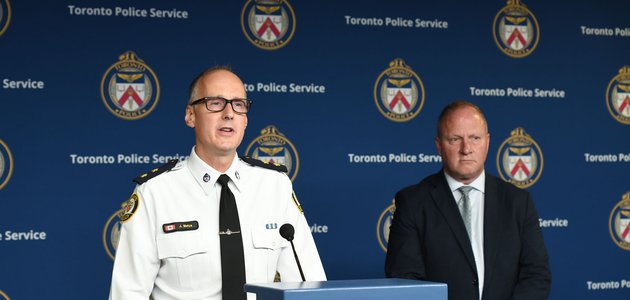 a man in a police uniform stands at a podium with another man in a business suiit next to him