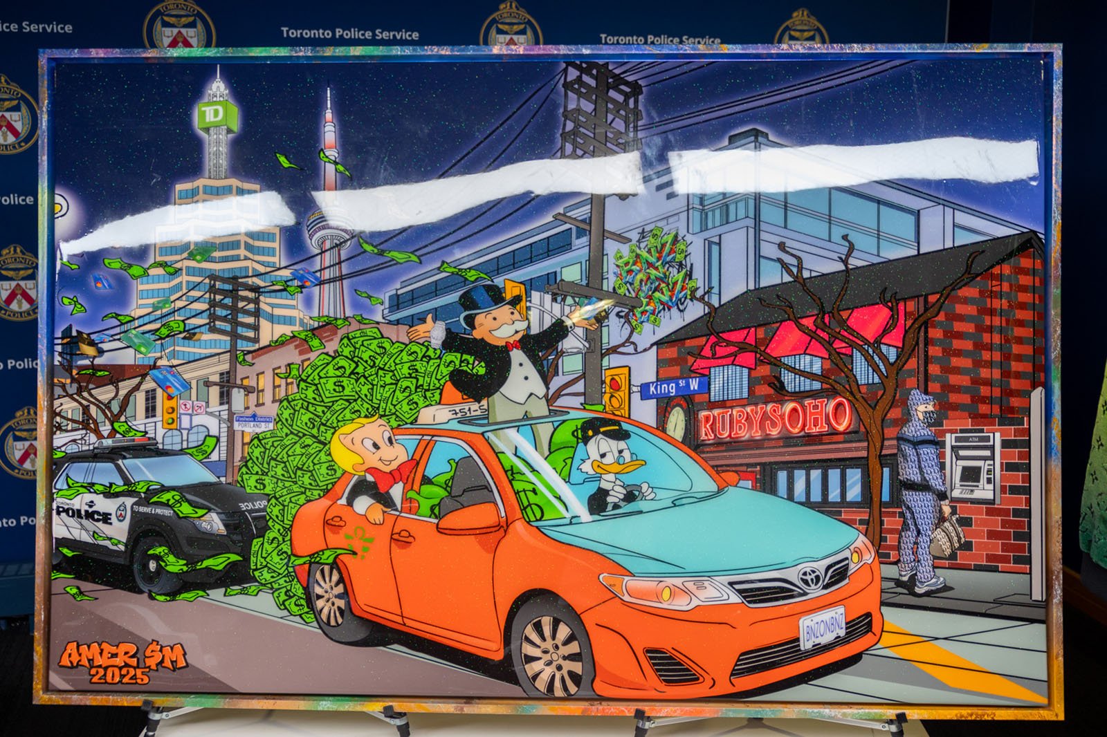 photo of an art piece featuring Mr. Monopoly riding in an orange taxi with dollar bills falling out of the trunk