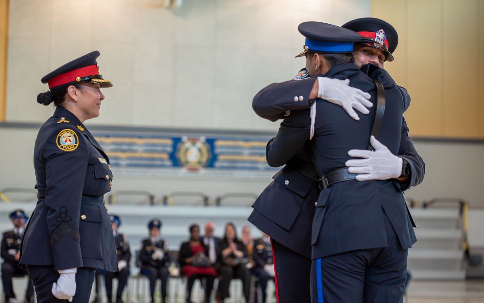 Woman in police uniform looks on as two man in police uniforms embrace