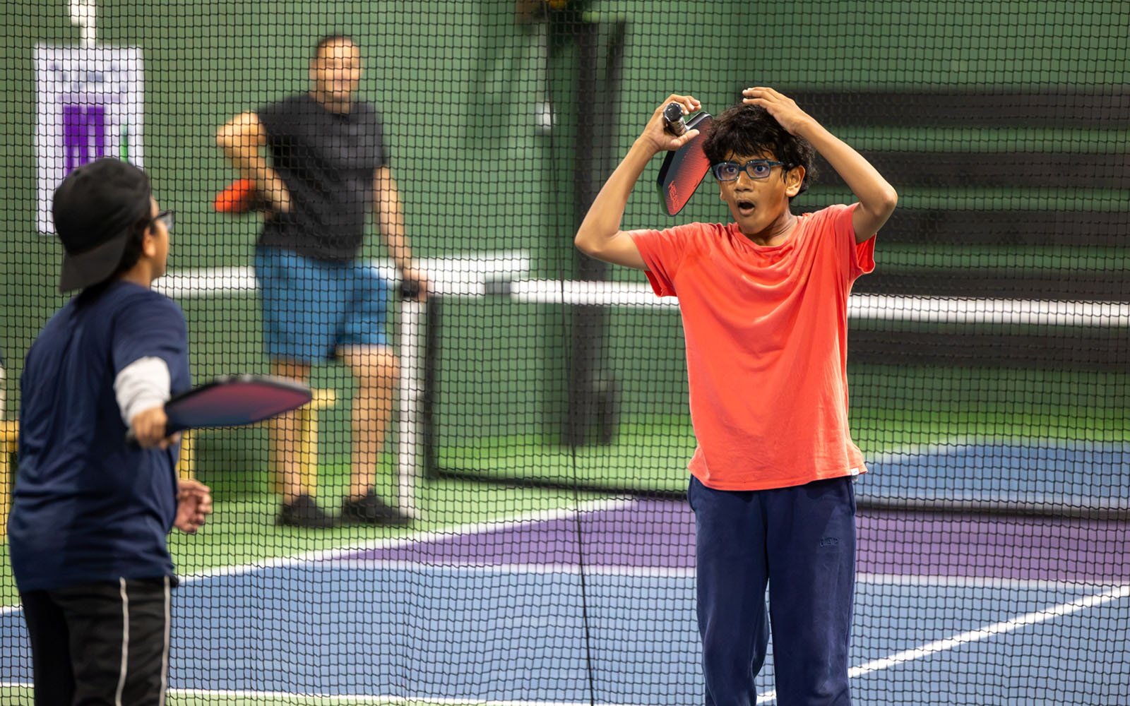 two boys looking at each other holding pickleball rackets inside a large playing field