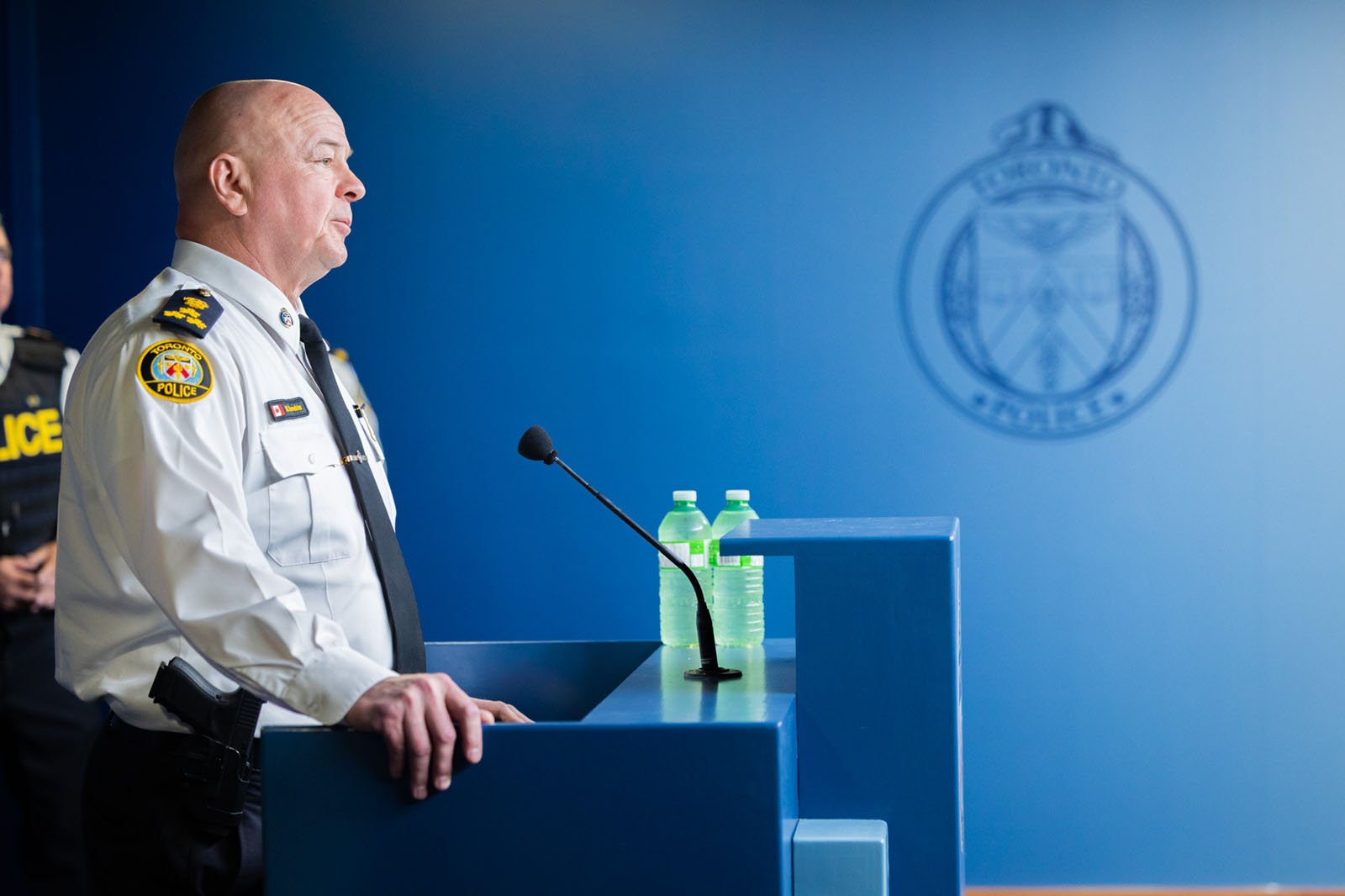 A side view of a man in a police uniform at a podium with a toronto police crest in the background