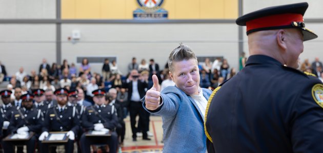A person giving a thumbs up to the camera with an audience behind them