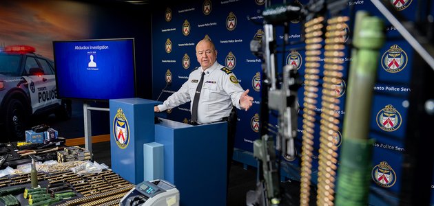 Police officer at a podium behind a display of weapons.