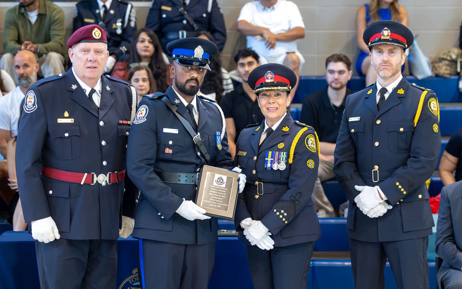 three men and a woman in police uniforms pose for a photo; man in the middle is holding an award plaque