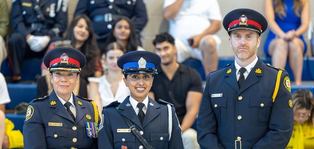 two women and a man in a police uniform stand infront of a crowd of people; woman in the middle is holding a plaque