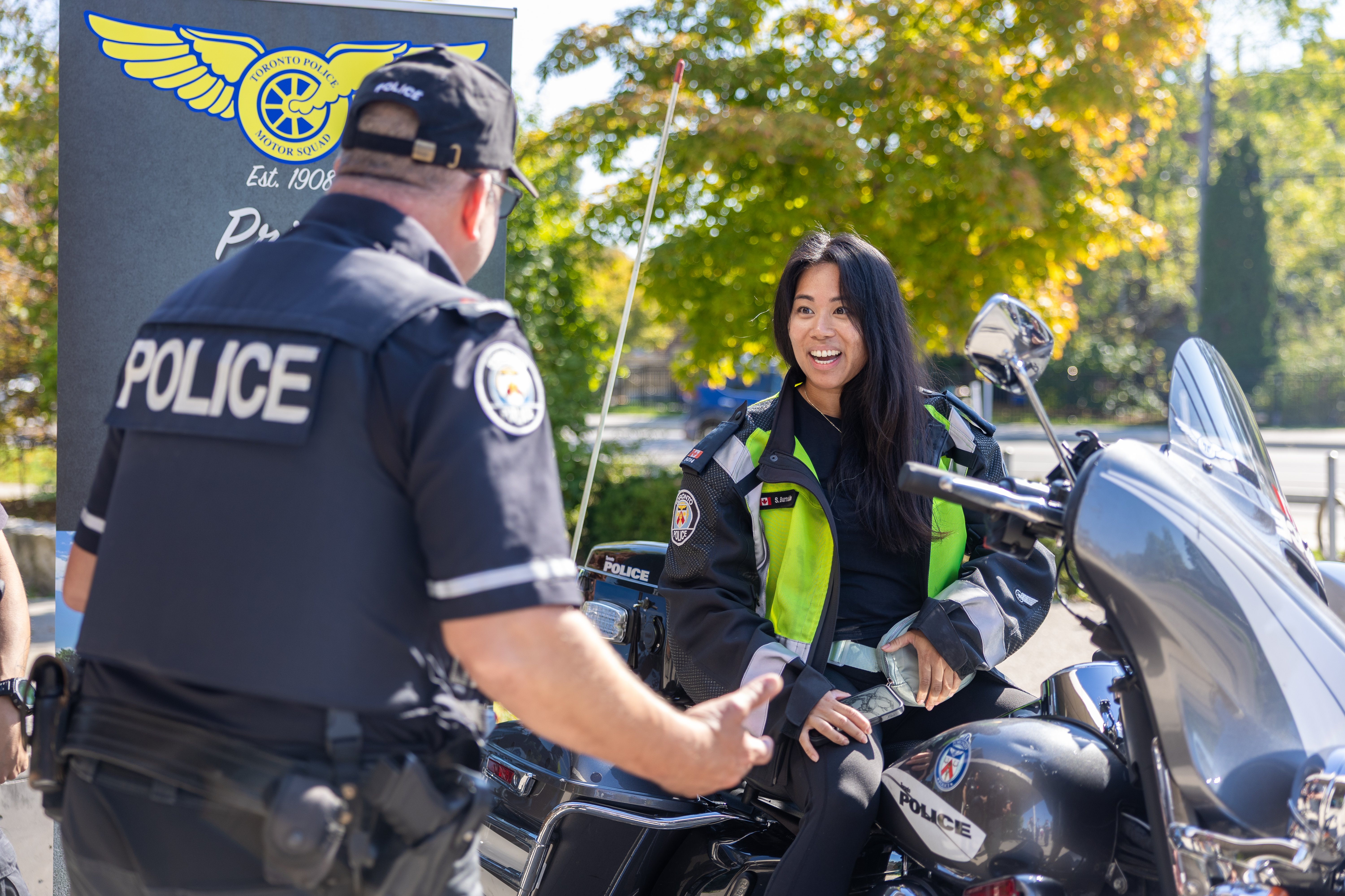 A smiling woman on a motorcycle facing a police officer