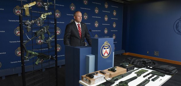Man at a podium behind a display of firearms