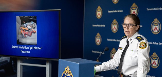 woman in a police uniform stands next to a TV screen which is displaying a photo of imitation firearms