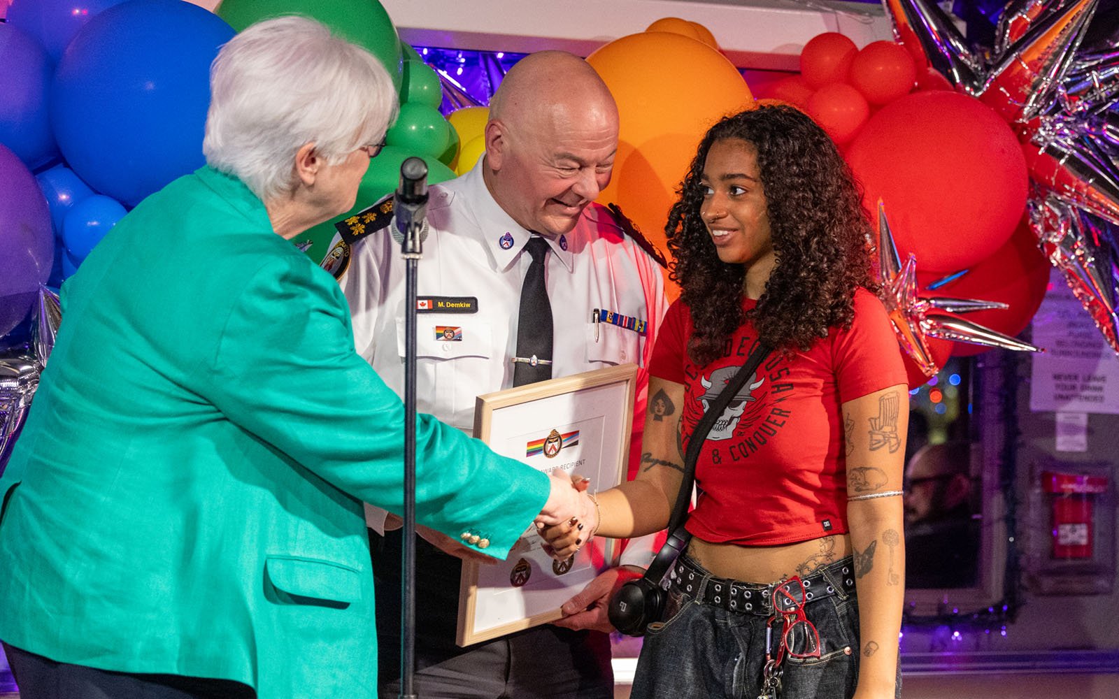 man in a police uniform is flanked by two women who are shaking hands