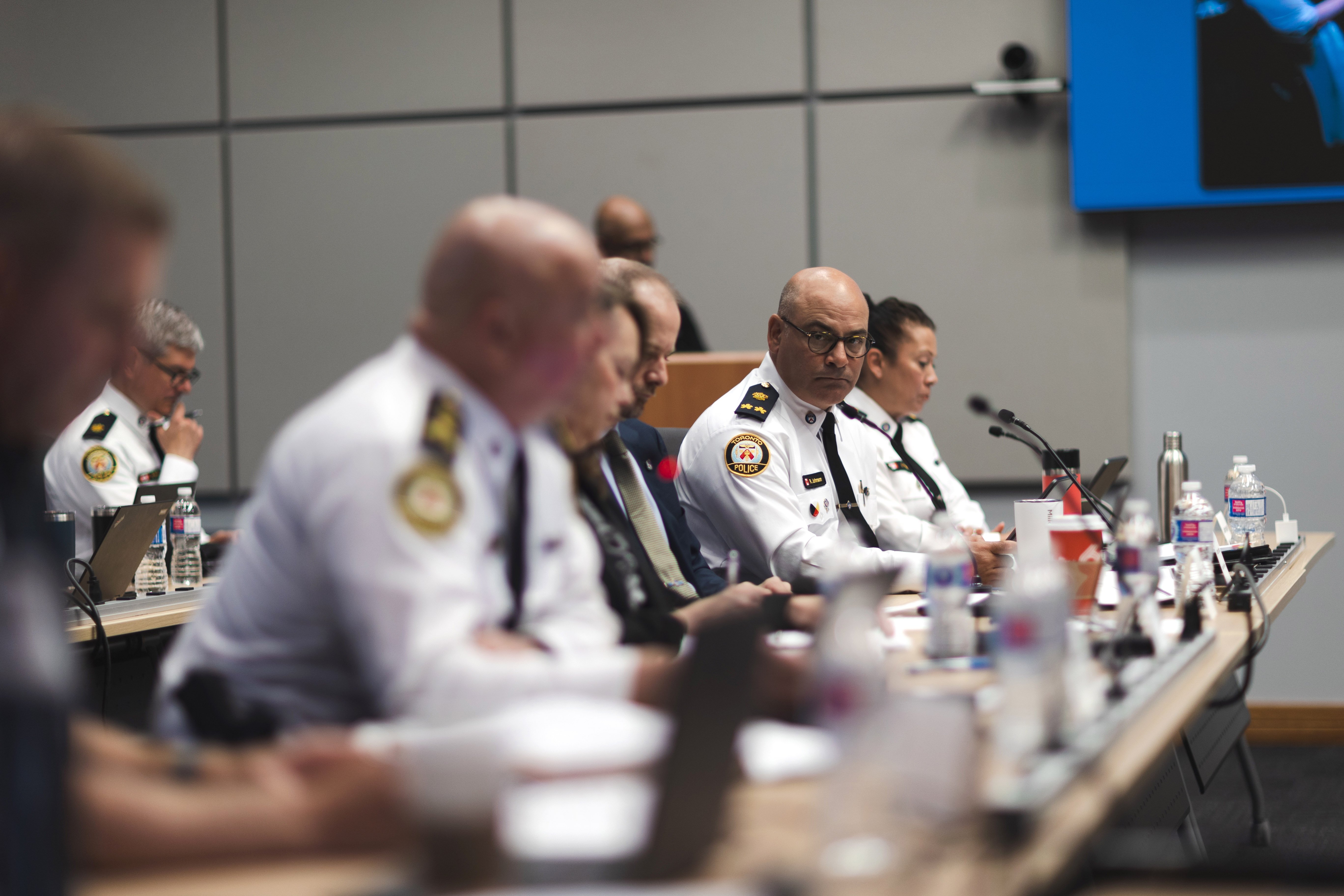 side view of a group of people in white shirts with yellow insignia sitting at a long table, all but one are out of focus
