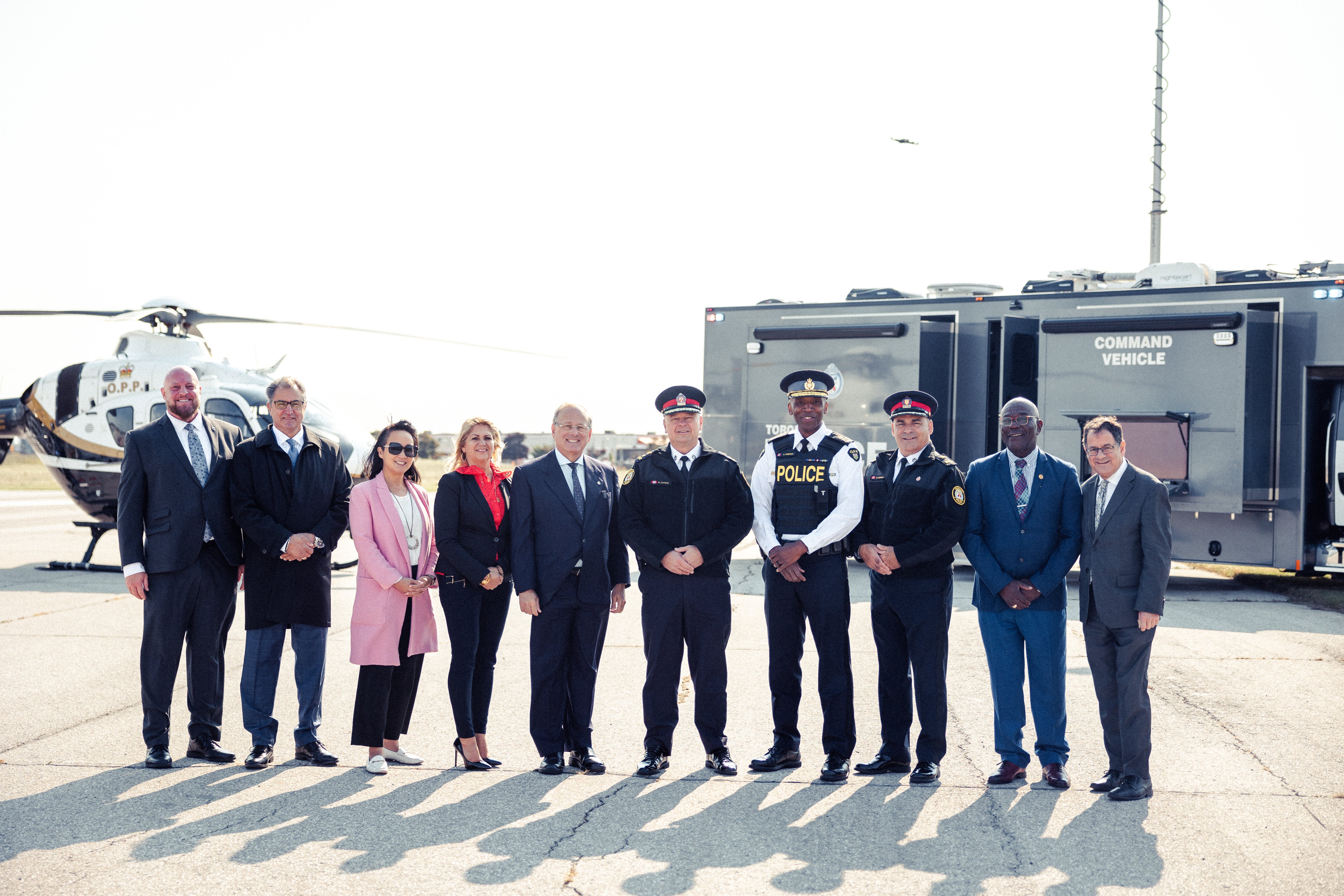 A line of people stand in front of a helicopter and command truck
