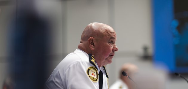 profile of a man wearing a white police shirt with yellow patches and insignia speaking