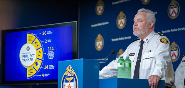 man in a police uniform standing at a podium with a TV screen in the background displaying a pie chart