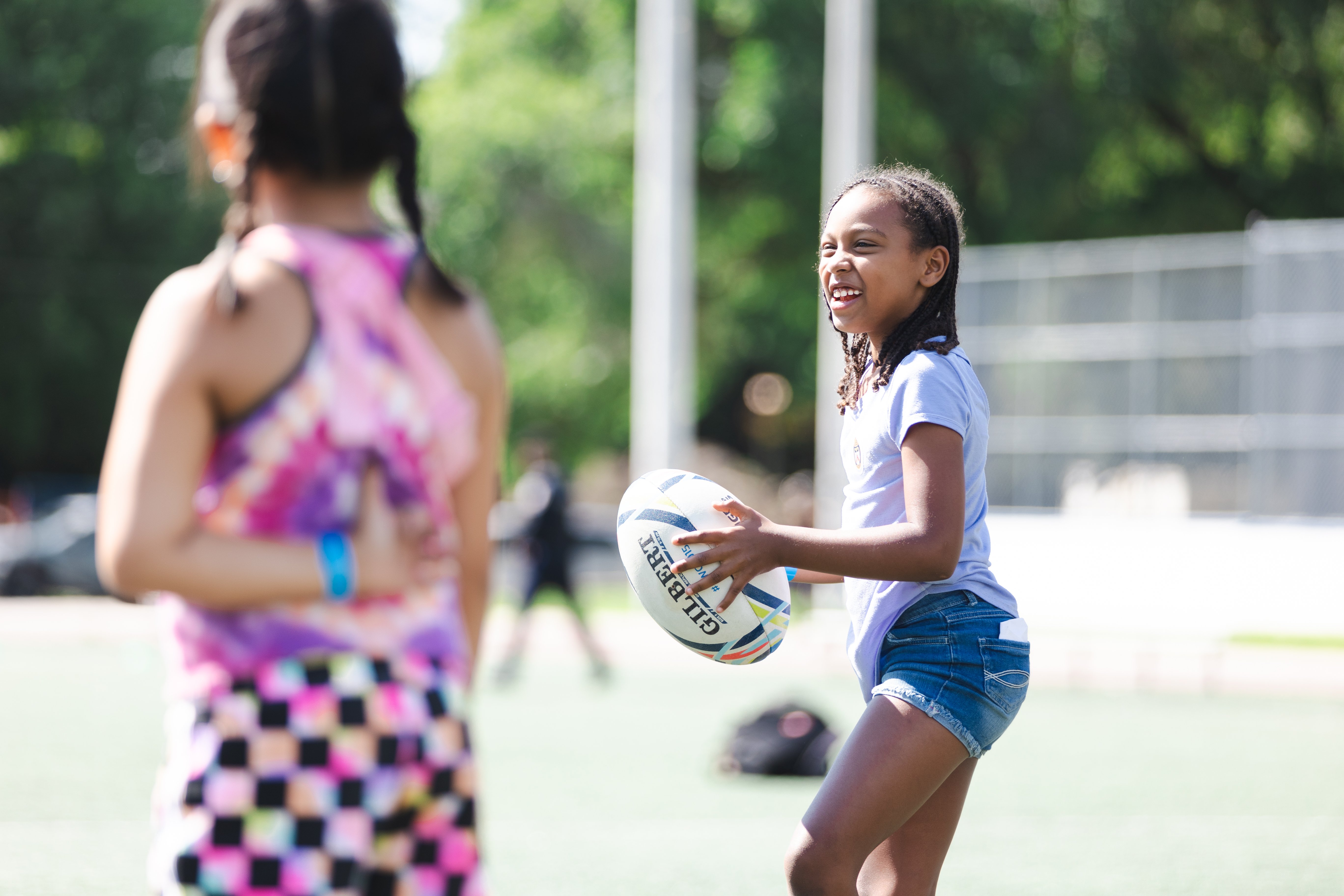 A girl holds a rugby ball and smiles