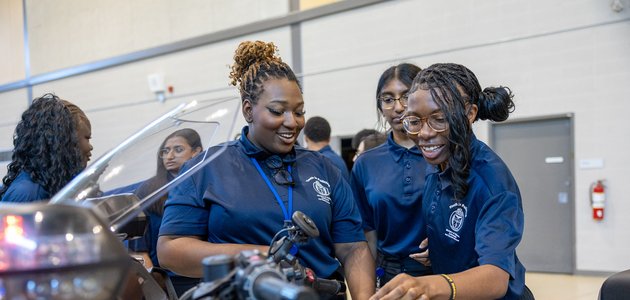 several students inside a gymnasium looking at a motorcycle