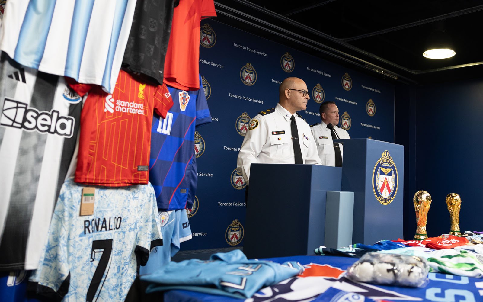 man in a police uniform stands infront of a podium with soccer jerseys hanging to his side