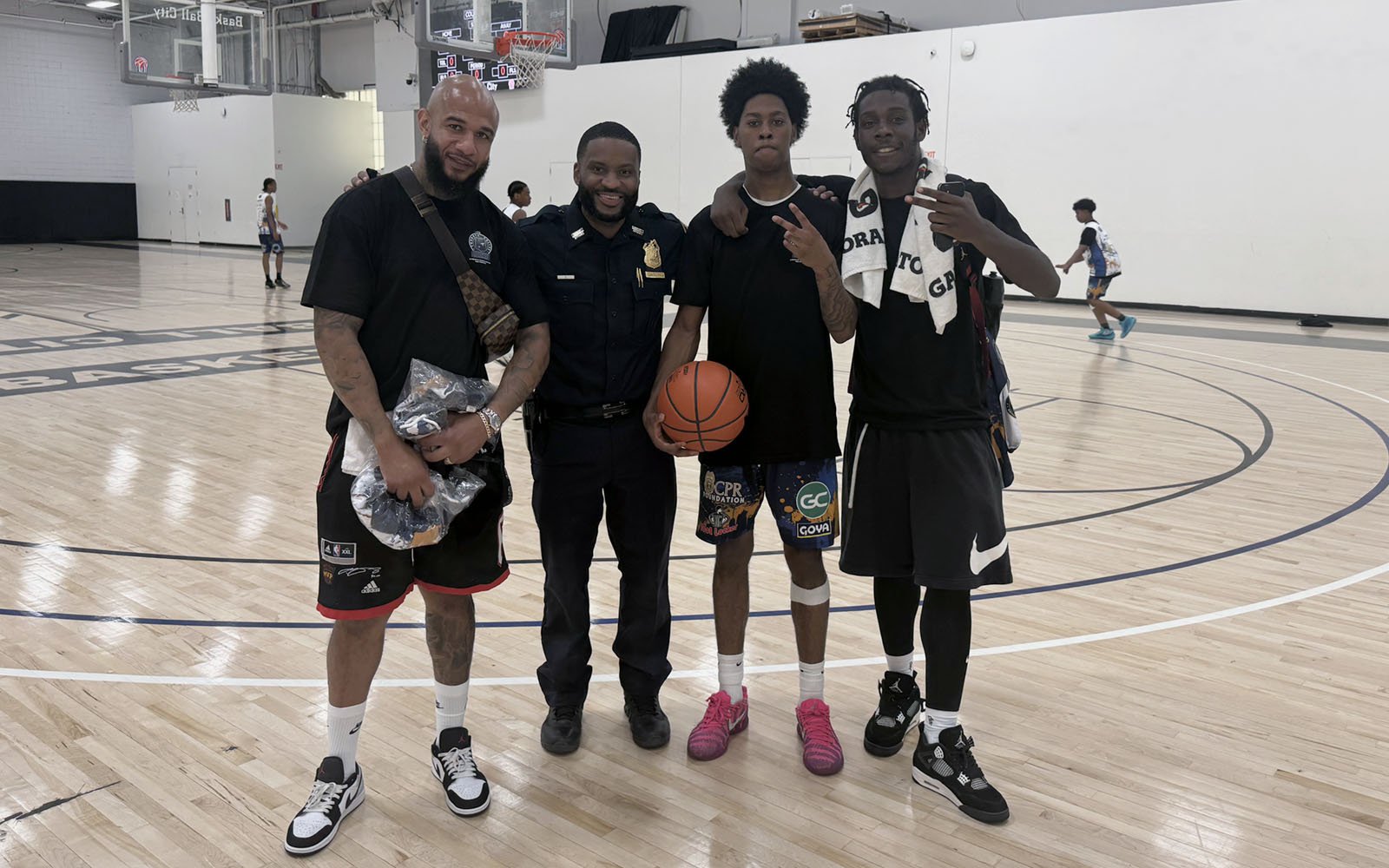 four men, one in a police uniform, stand inside an indoor basketball course