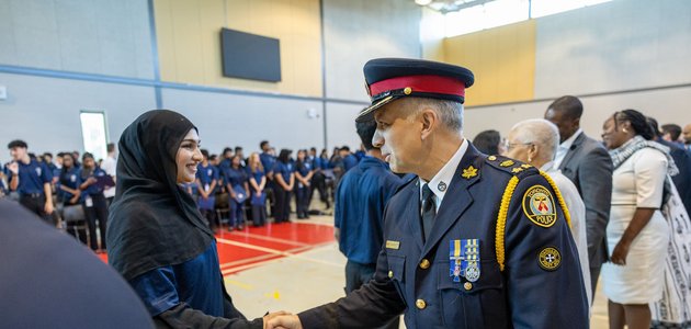 man in a police uniform is shaking a hand of a female student wearing a hijab