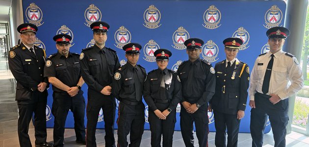group of men and women in police uniforms standing in front of a backdrop wall with toronto police service crest pattern on it
