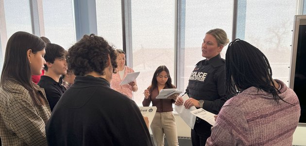 Police officer speaking to a group taking notes.