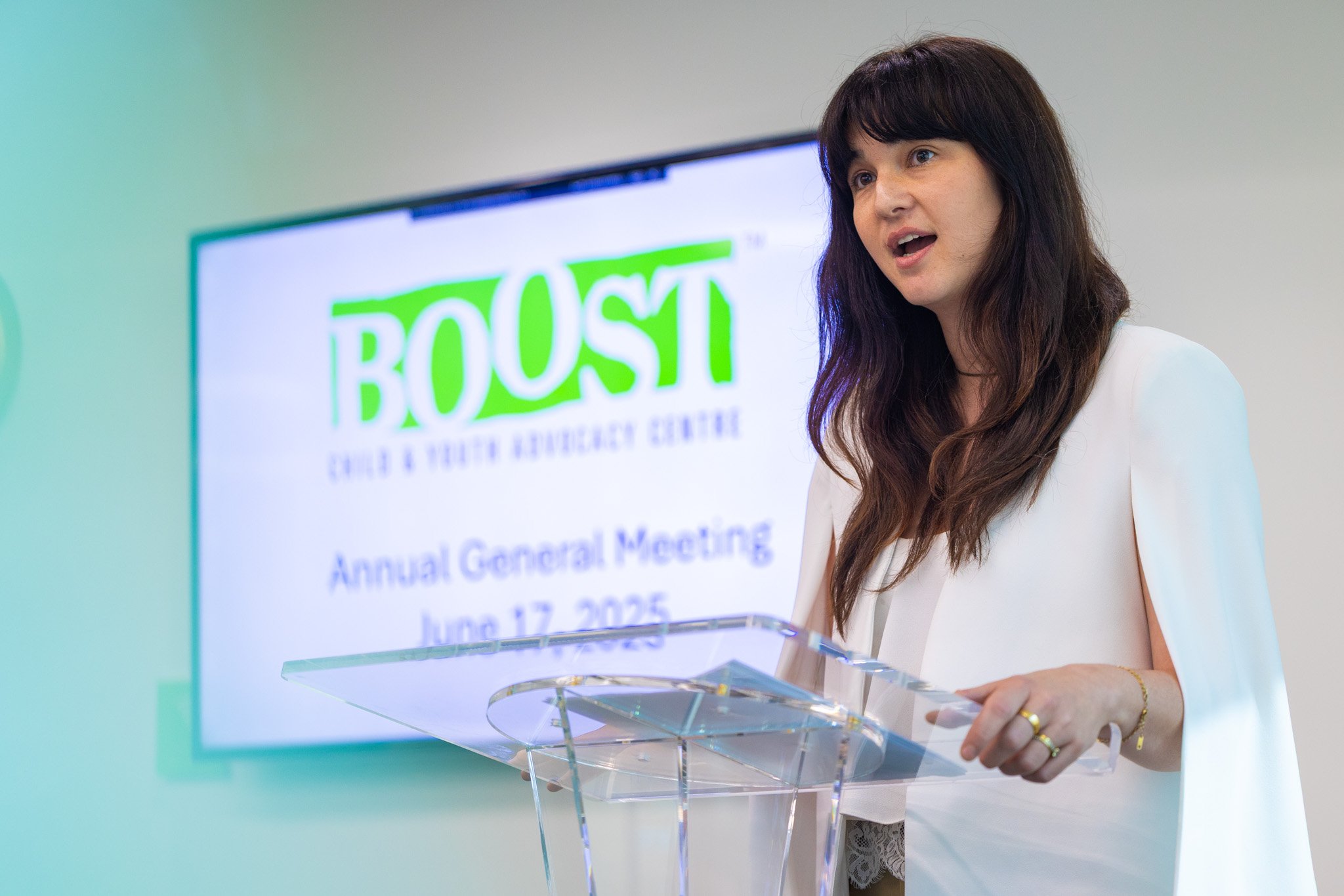 Woman standing in front of a podium with a TV screen behind her showing a BOOST logo