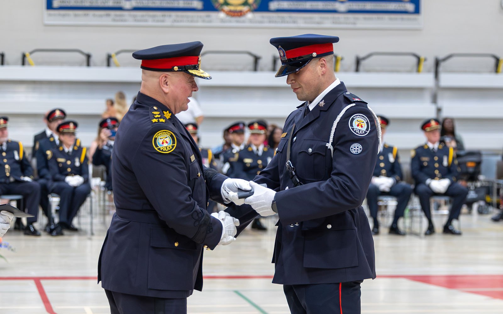 two men in police uniforms stand inside a large gymnasium hall