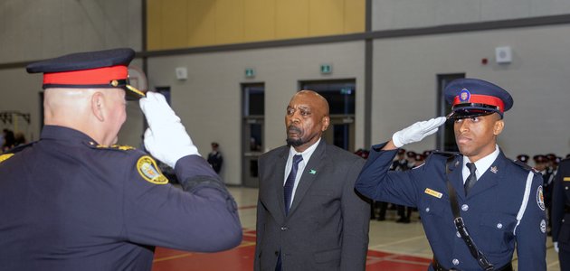 two men in police uniforms saluting, while a man in the middle in business suit stands still