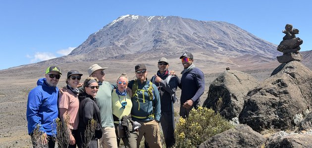 group of men and women posing outdoors with a tall mountain behind them