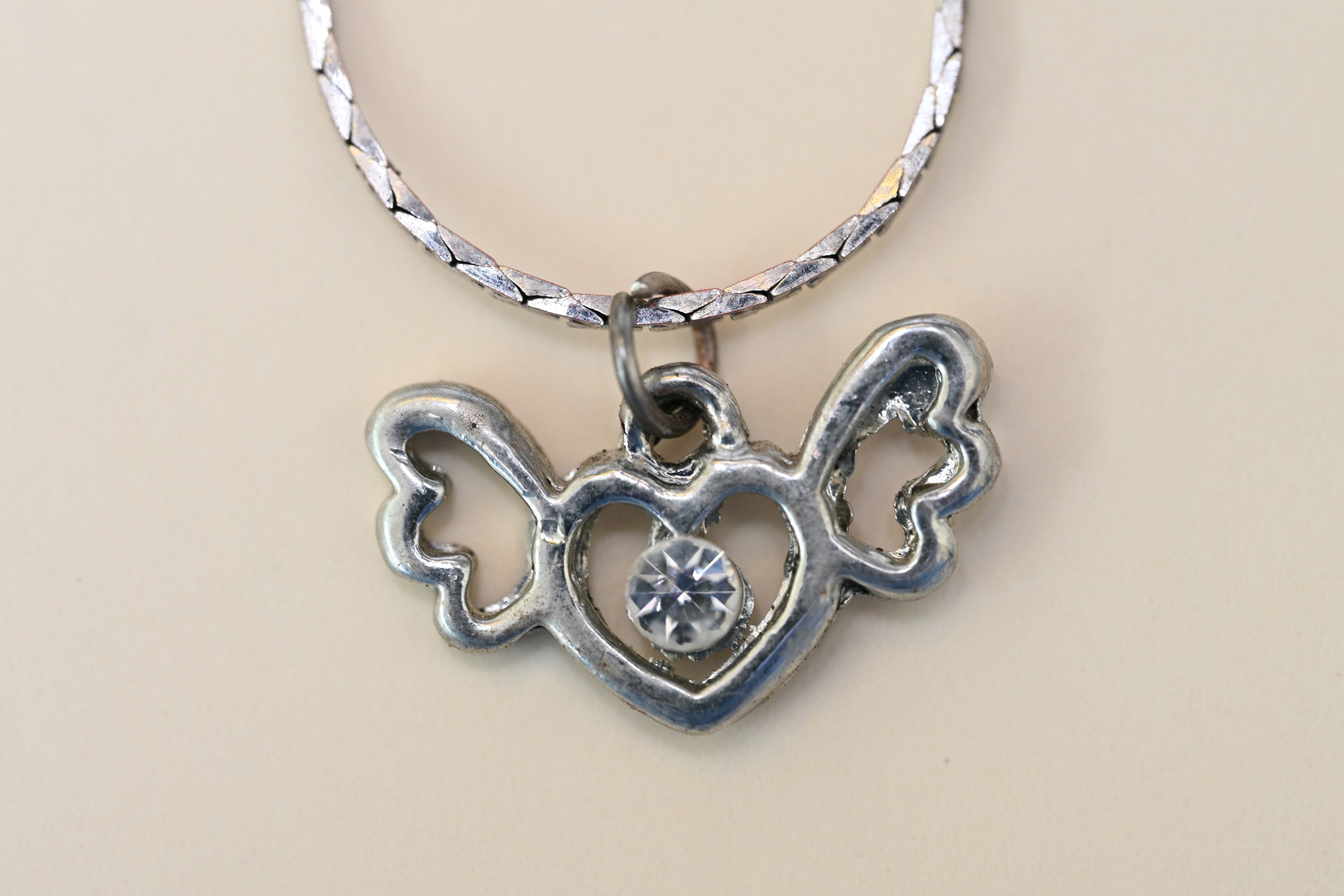 Necklace worn by victim with a silver heart-shaped pendant with wings and a single clear stone in the centre